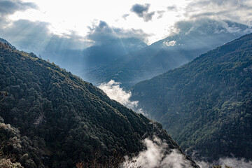 mountain valley covered with dense cloud and bleeding sun rays at morning from flat angle