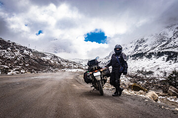 girl solo ridder in ridding gears with loaded motorcycle at isolated road and snow cap mountains