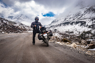 man solo ridder in ridding gears with loaded motorcycle at isolated road and snow cap mountains