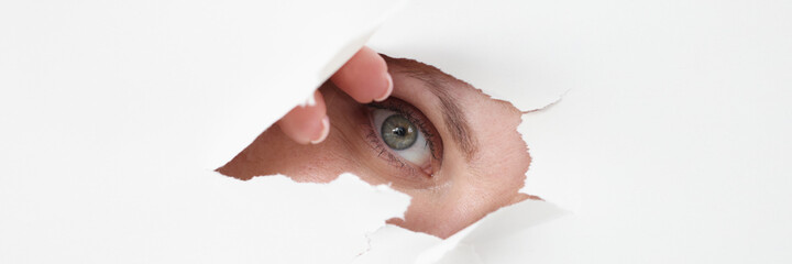 Female eye looks through hole in white paper © H_Ko