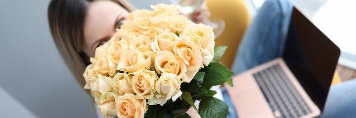 Woman holds large bouquet of roses anda glass of wine on her lap is laptop