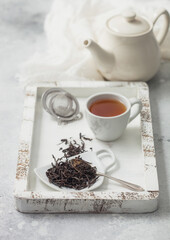 Black loose tea with tea ball strainer infuser and ceramic teapot with cup in wooden box with white linen cloth.