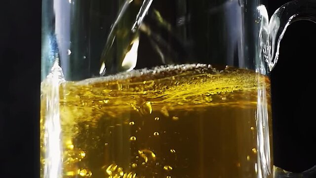 Beer is pouring into a beer mug with bubbles on a black background. 4k slow motion video with the camera moving down.