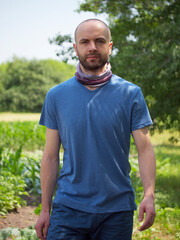 A self-confident bald man with facial hair walks among the plants in summer. A confident, purposeful look. Portrait.