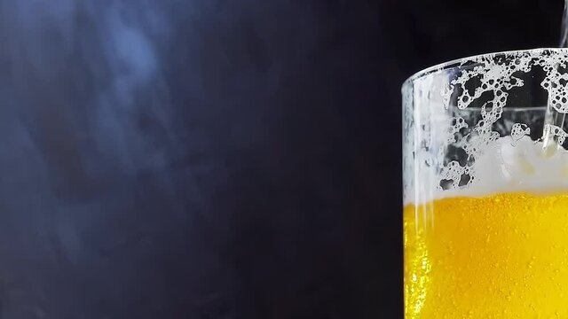 Beer is pouring into a beer mug with bubbles close-up on a black background. Overflowing beer glass with flowing foam. 4k slow motion video 60 fps with camera movement to the right.