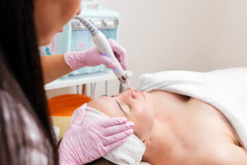 Beauty salon. The cosmetologist in medical gloves makes a hydra peeling procedure for the client in...