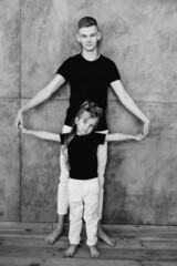 stylish caucasian siblings (brother and sister) in black t-shirts and white pants standing by the gray wall in loft interior. Family, fashion, relatives, relationship and children concept.