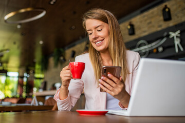 Young woman enjoying a cup of coffee. Portrait of a young beautiful businesswomen enjoying coffee during work on portable laptop computer, charming female student using net-book while sitting in cafe