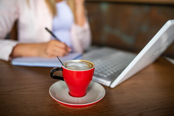 Close up of a woman hold a pencil taking notes and drinking coffee at the café. Closeup hands of Freelancer woman working using digital laptop computer and drink coffee on cafe table at cafe shop