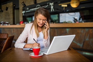 Young woman enjoying a cup of coffee. Portrait of a young beautiful businesswomen enjoying coffee during work on portable laptop computer, charming female student using net-book while sitting in cafe