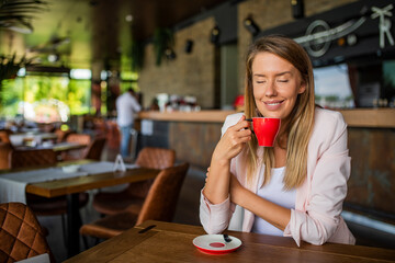 Thoughtful woman sitting in cafeteria holding coffee mug while looking away. Woman drinking tea while thinking. Relaxing and thinking while drinking coffee. Happy Nice Lady Drinking Coffee
