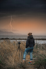 Woman photographing lightning with a digital mirrorless camera on a tripod