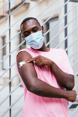 vertical portrait of an african young man. He is proud showing arm after vaccination
