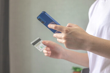 Woman use mobile phone for order online and pay bills with credit card in living room interior at home. Smartphone and credit card in hand closeup