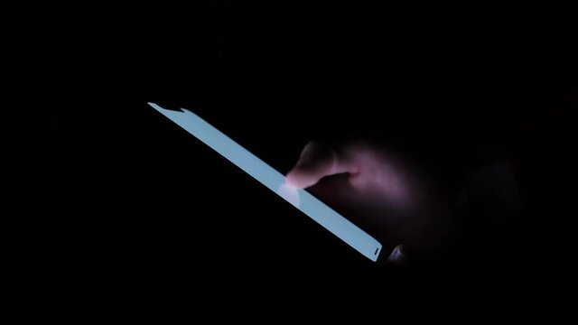 Close-up holding and using a smartphone in a dark room, white glowing screen.