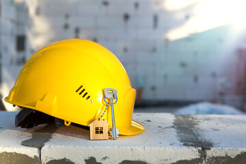 Construction yellow hardhat and key to house on window of housing made of blocks of porous...