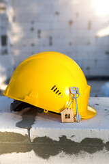Construction yellow hardhat and key to house on window of housing made of blocks of porous...