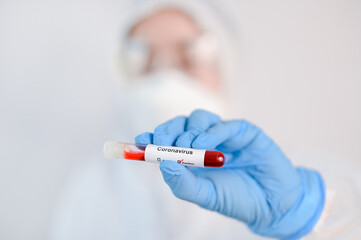 Selective focus of Corona virus blood sample in doctor hand in PPE suit.