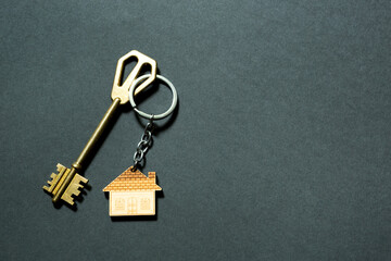 Key chain in the shape of house with key on a black background. Building, design, project, moving to new home, mortgage, deposit, rent and purchase real estate. Copy space