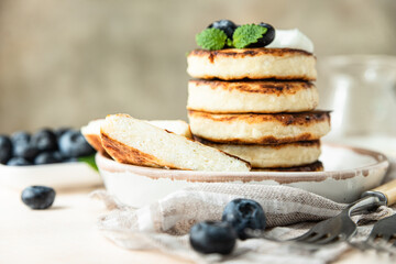 Fried cottage cheese pancakes or fritters with blueberry and sour cream on a plate. Gluten free. Traditional breakfast of Ukrainian and Russian cuisine.