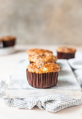 Tasty breakfast muffins with oat crumbs topping on white cutting board, light concrete background.