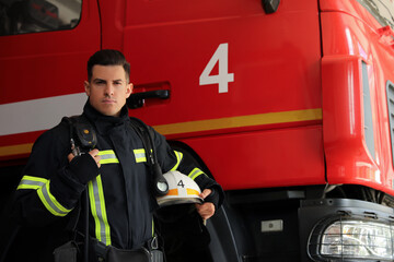 Portrait of firefighter in uniform with helmet near fire truck at station, space for text