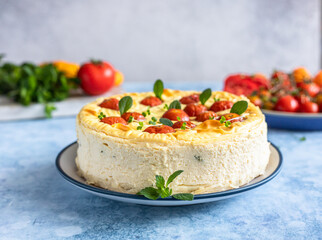Savoury cheesecake with tomatoes decorated with mint, blue concrete background.