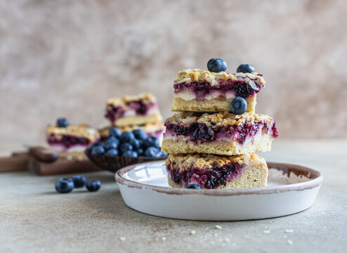 Crumble cheesecake bars with blueberry filling and fresh blueberries, concrete background. Bar slices with cheesecake, blueberry and streusel.