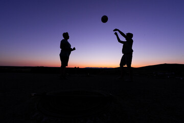 SILHOUETTE OF TWO CHILDREN AT SUNSET PLAYING BALL.