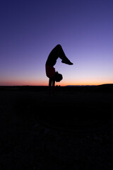 silhouette of a teenage girl doing gymnastics and jumping jacks at sunset.