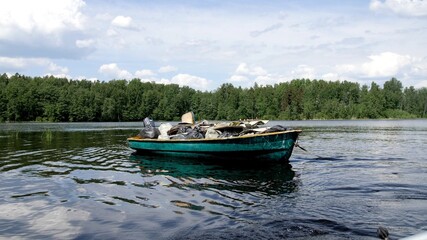 Fototapeta na wymiar A boat full of garbage floats on the lake. Waste transportation. White clouds in the blue sky. Sunny summer weather. Waste for recycling. Cleaning forests and islands. Environmental protection 