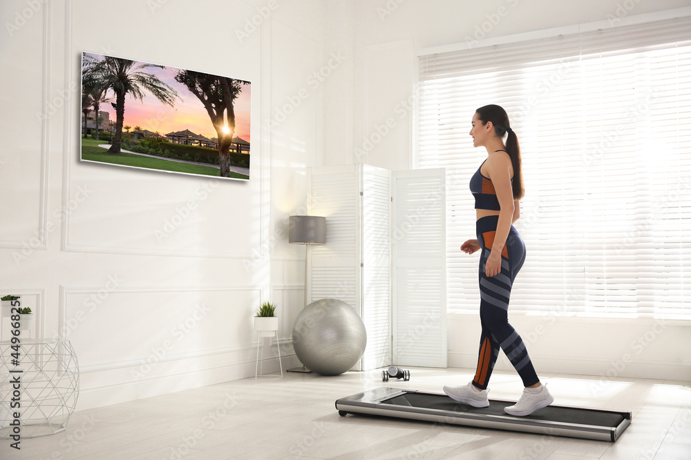 Sticker sporty woman training on walking treadmill and watching tv at home