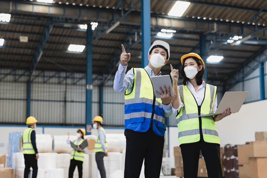 Factory manager and female engineer or staff in  medical mask and safety protective suite using computer laptop and digital tablet working discuss together