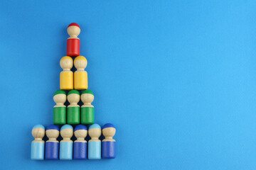 pyramid of multicolored wooden toy people on blue background with copy space, concept of social...