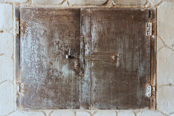 An old unpainted iron oven door in a rustic stone stove. Two leaves are closed with a locking device. there are traces of rust on the metal surface and scratches from cleaning. Background. Texture.