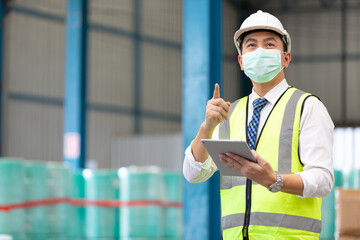 male factory worker wearing medical face mask, pointing to something and using tablet in factory