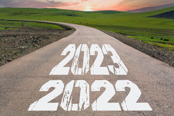 New year 2022, 2023 written on country road with tree tunnel on side in the mountains in summer. Road to success concept and business recovery challenge idea