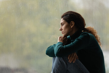 Side view frustrated thoughtful woman looking out rainy window in distance alone, lost in thoughts,...