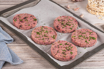 Raw veggie burger with beetroot and white beans with parsley leaves on wood cutting board.