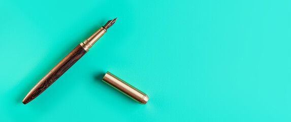 Wooden and gold fountain ink pen, opened, cap on the right, blue green background top down view,...