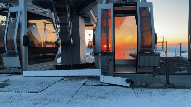 Comfortable gondolas of modern poma lift move to station at popular ski resort at picturesque sunset on snowy mountain slope