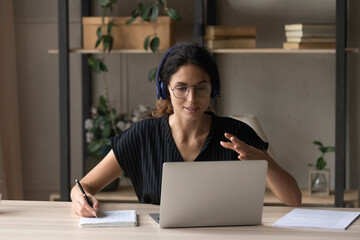 Close up woman in headphones and glasses leading online lesson, using laptop, taking notes, studying, teacher coach explaining, smiling businesswoman consulting client, involved in internet meeting