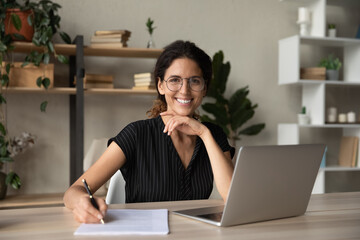 Head shot portrait of smiling woman in glasses writing, taking notes, female student sitting at...