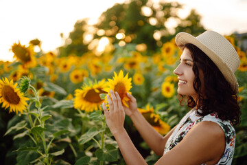 Beautiful  woman strolling through field with sunflowers at sunset.  Rural happy life. Nature, relax and lifestyle.