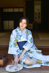 古民家の縁側にたたずむ浴衣姿の若い女性