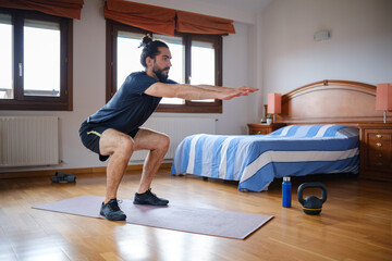 Sporty bearded man doing squats while training at home.