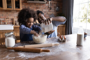 Happy young African American father and cute excited teen daughter have fun bake cookies pie at...