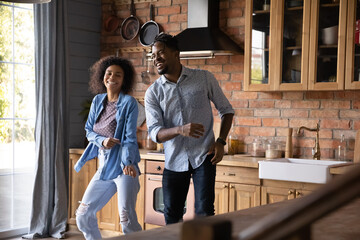 Obraz premium Excited millennial African American man and woman have fun dance together in home kitchen. Smiling young ethnic couple renters enjoy relocation moving to new house. Rental, real estate concept.