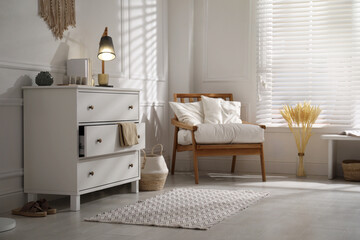 Obraz premium Stylish room interior with white chest of drawers and comfortable armchair