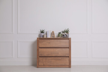 Books and beautiful plants on wooden chest of drawers near white wall indoors